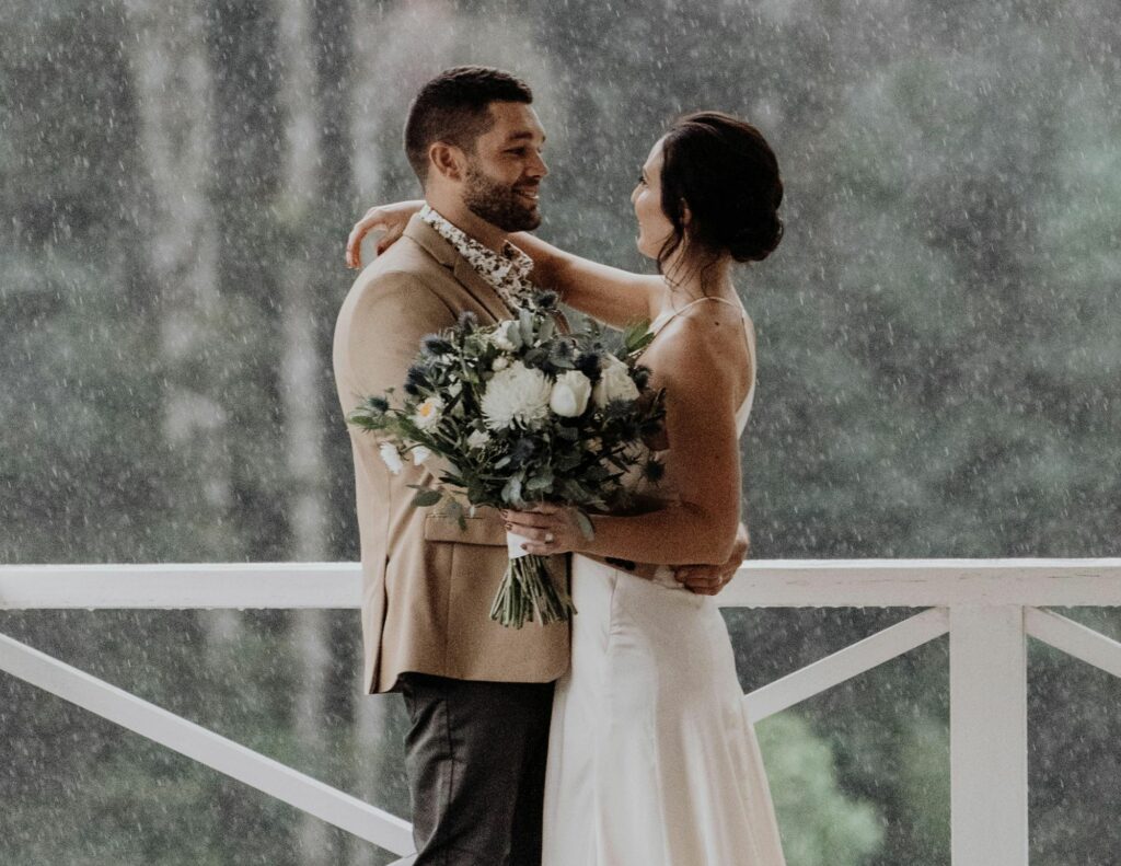 Newlyweds posing with rain in the background, showing that even in the rain, a wedding remains magical.