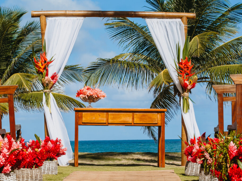 Colorful arch decorated with exotic flowers and tropical foliage, with palm trees and the Caribbean Sea on the horizon