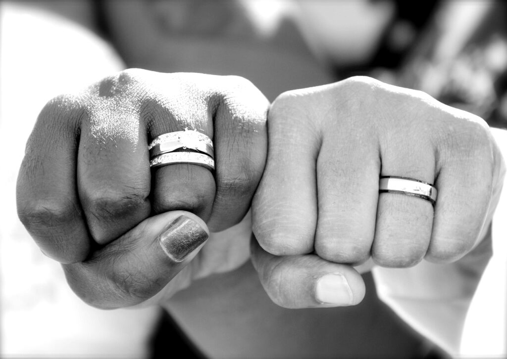 Two newlyweds’ hands side by side, fists clenched and wedding rings visible, symbolizing their unity and shared strength to overcome wedding stress.
