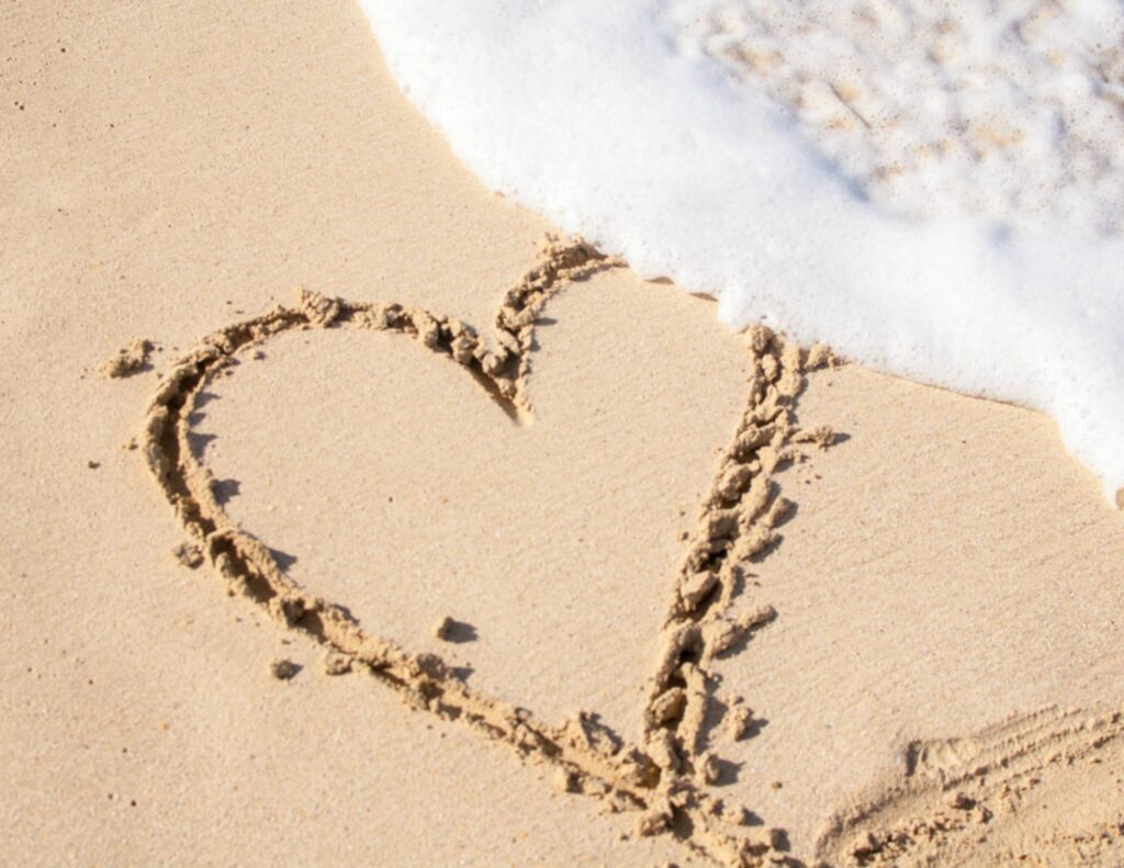 A heart drawn in the sand, gently touched by a wave, capturing a romantic moment on the beach.